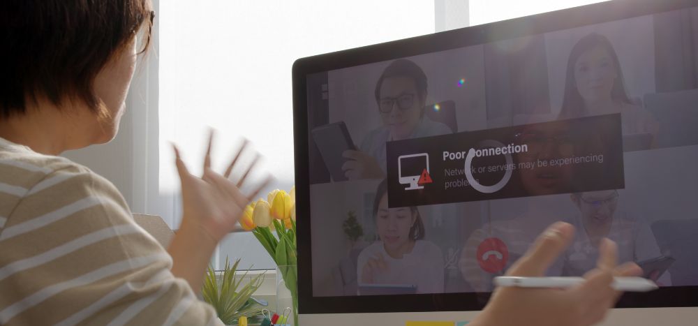 Signs your business broadband is holding you back: A person viewed from behind raises their hands in frustration at a desktop monitor displaying a "Poor Connection" error message during a video call with colleagues.